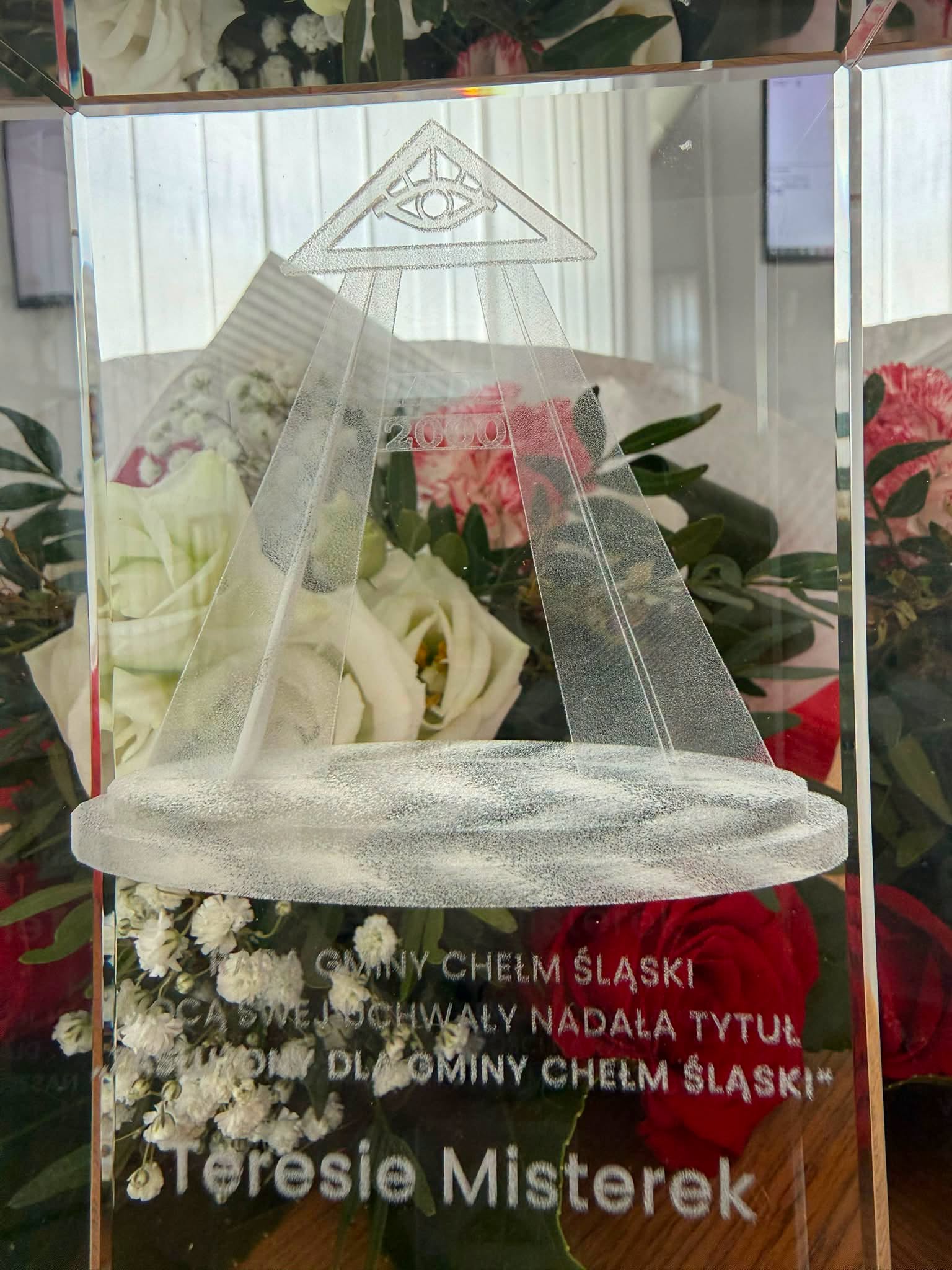 Szklana statuetka za nią kwiaty. 