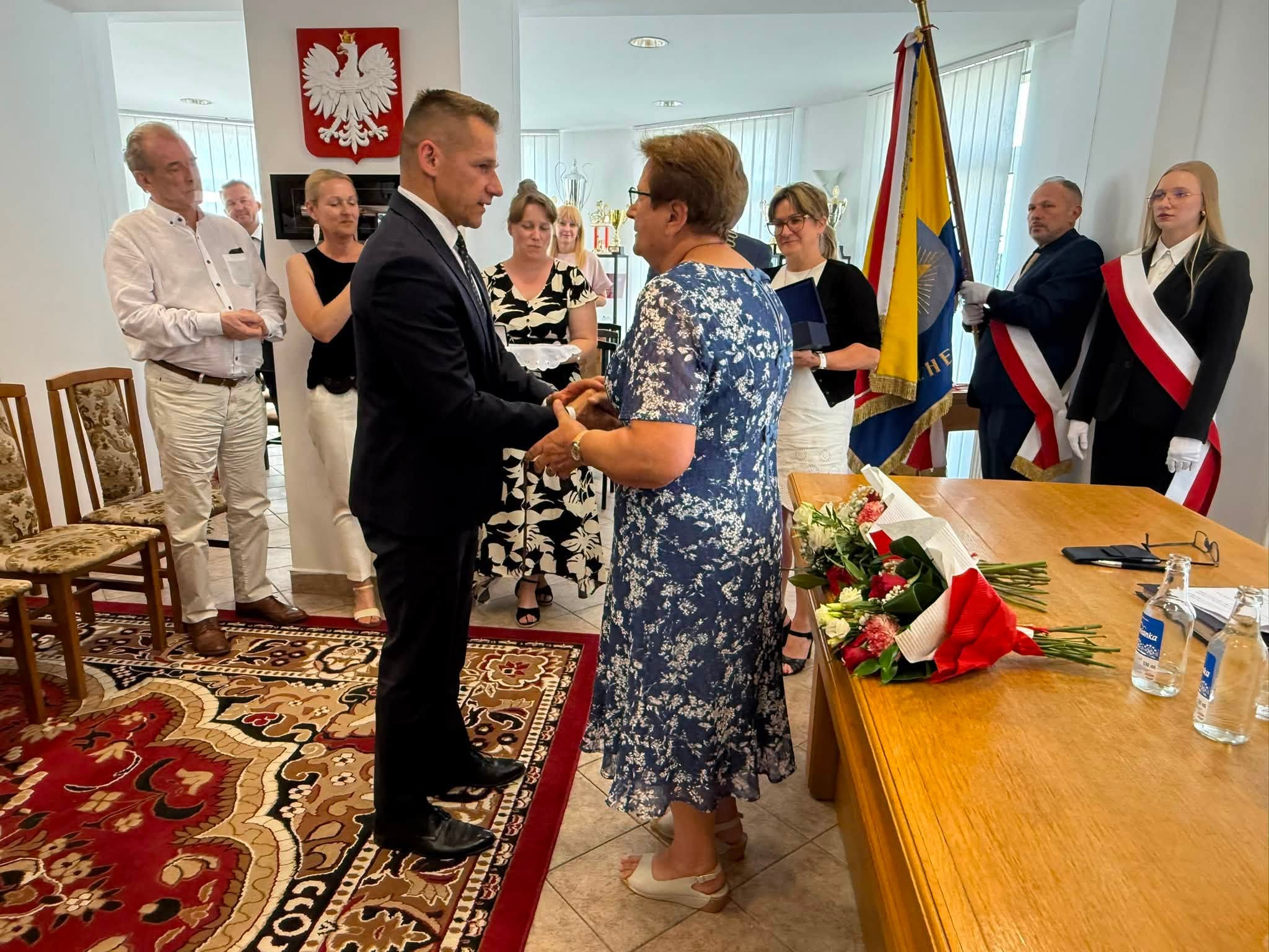 Mężczyna składający serdeczne gratulacje i słowa uznania w pomieszczeniu. W tle stojące osoby. 