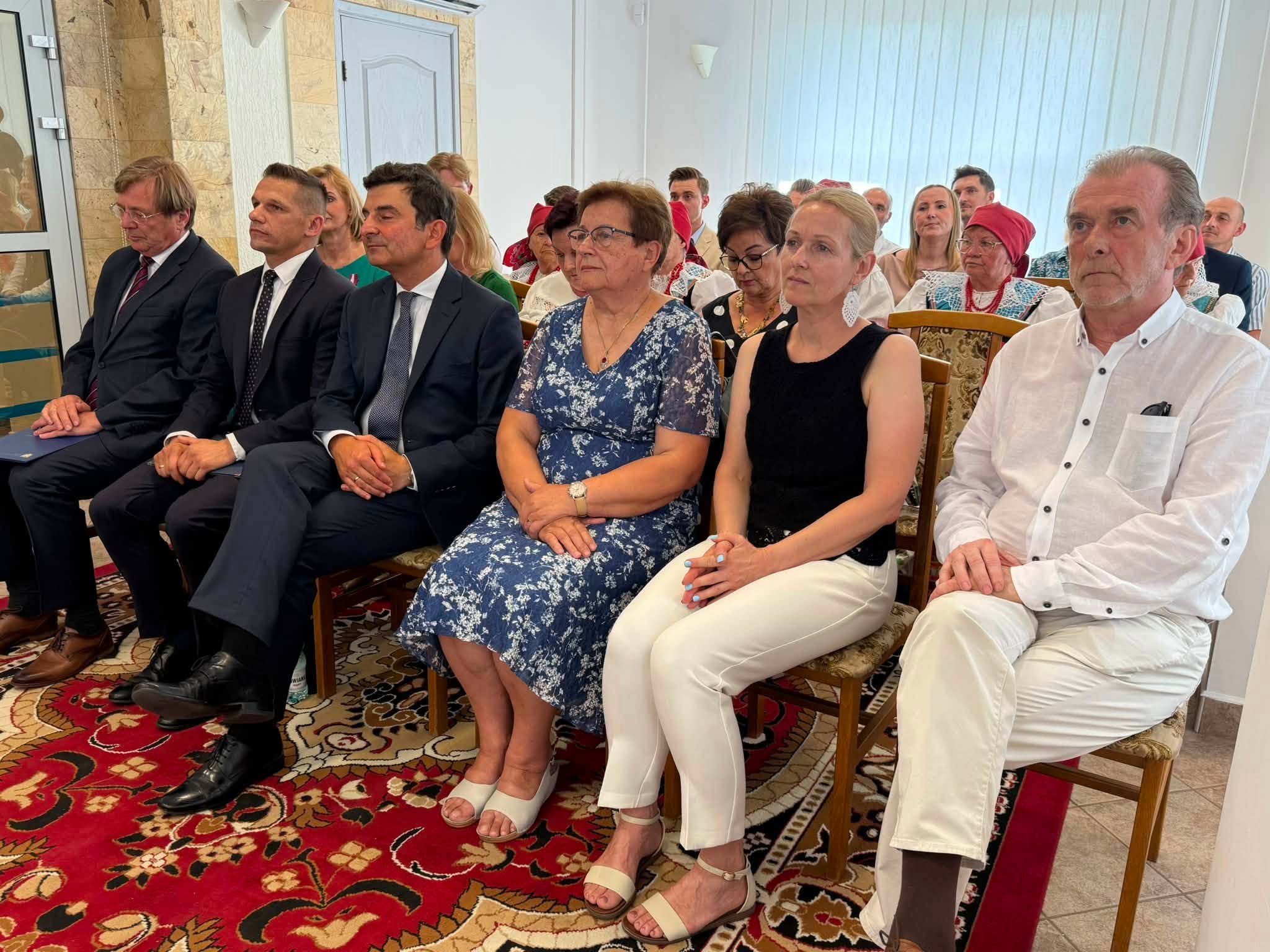 Osoby siedzące w pomieszczeniu na krzesłach w ustawieniu kinowym. 