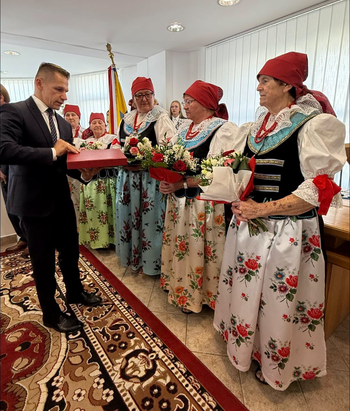 Mężczyzna wręczający paniom w strojach ludowych grawerton. 
