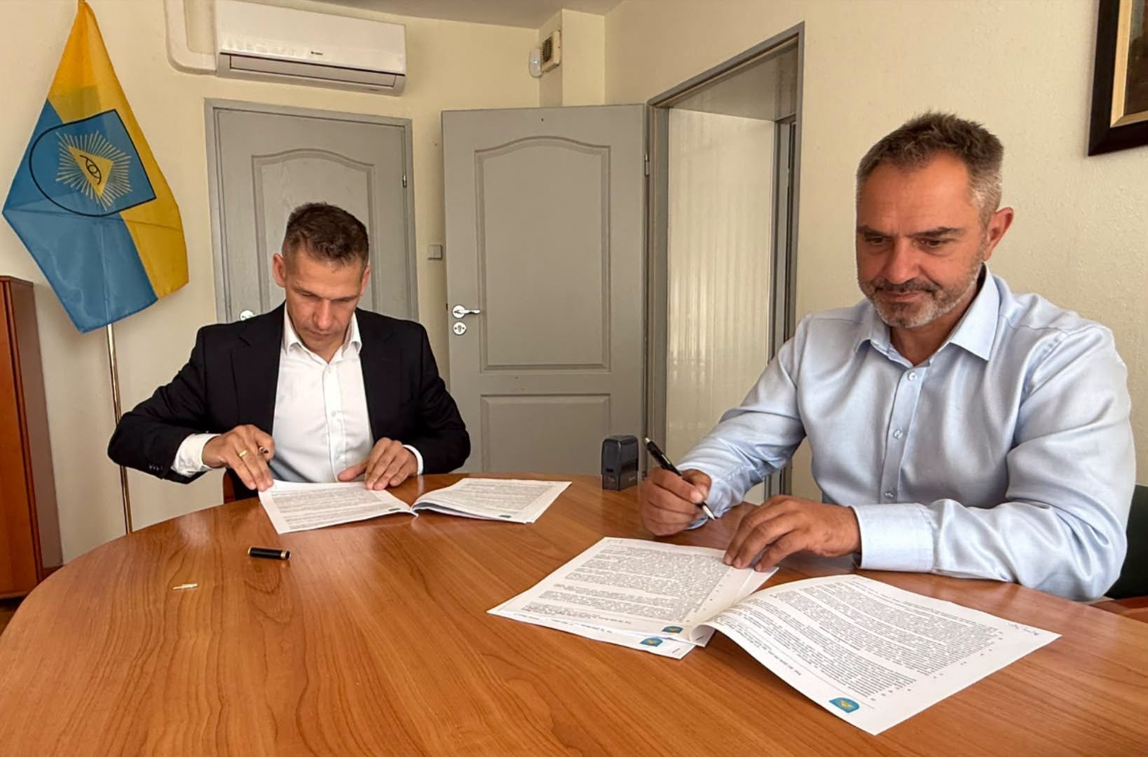 Dwaj mężczyźni podpisują umowę na realizację zadania w pomieszczeniu 