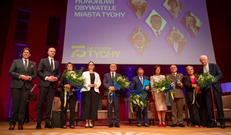 Osoby pozujące do zdjęcia na scenie w sali. 