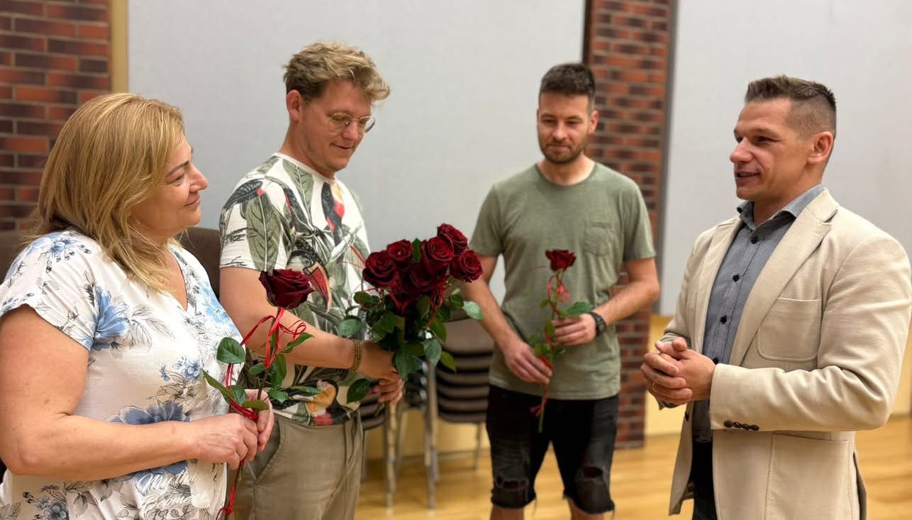 Trzech mężczyzn i kobieta w pomieszczeniu trzymający róże w dłoniach. 
