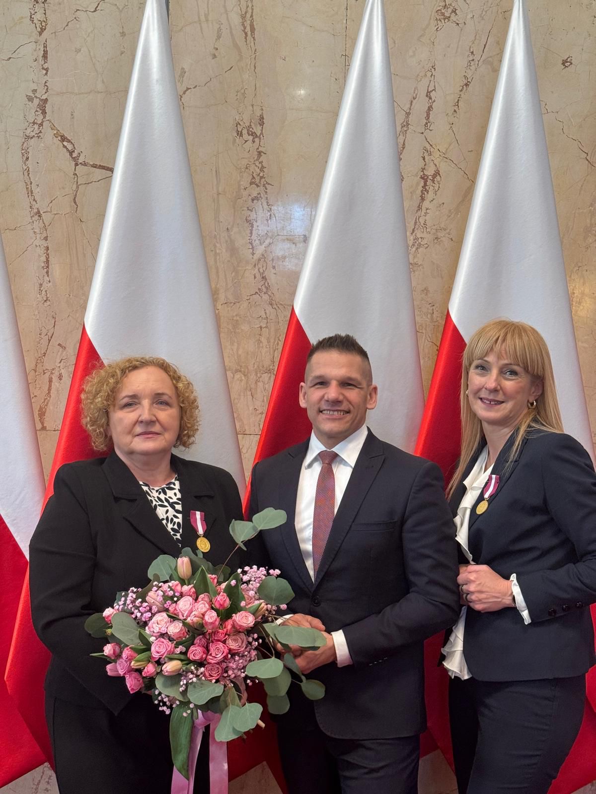 Trzy osoby pozujące do zdjęcia na tle flag. 