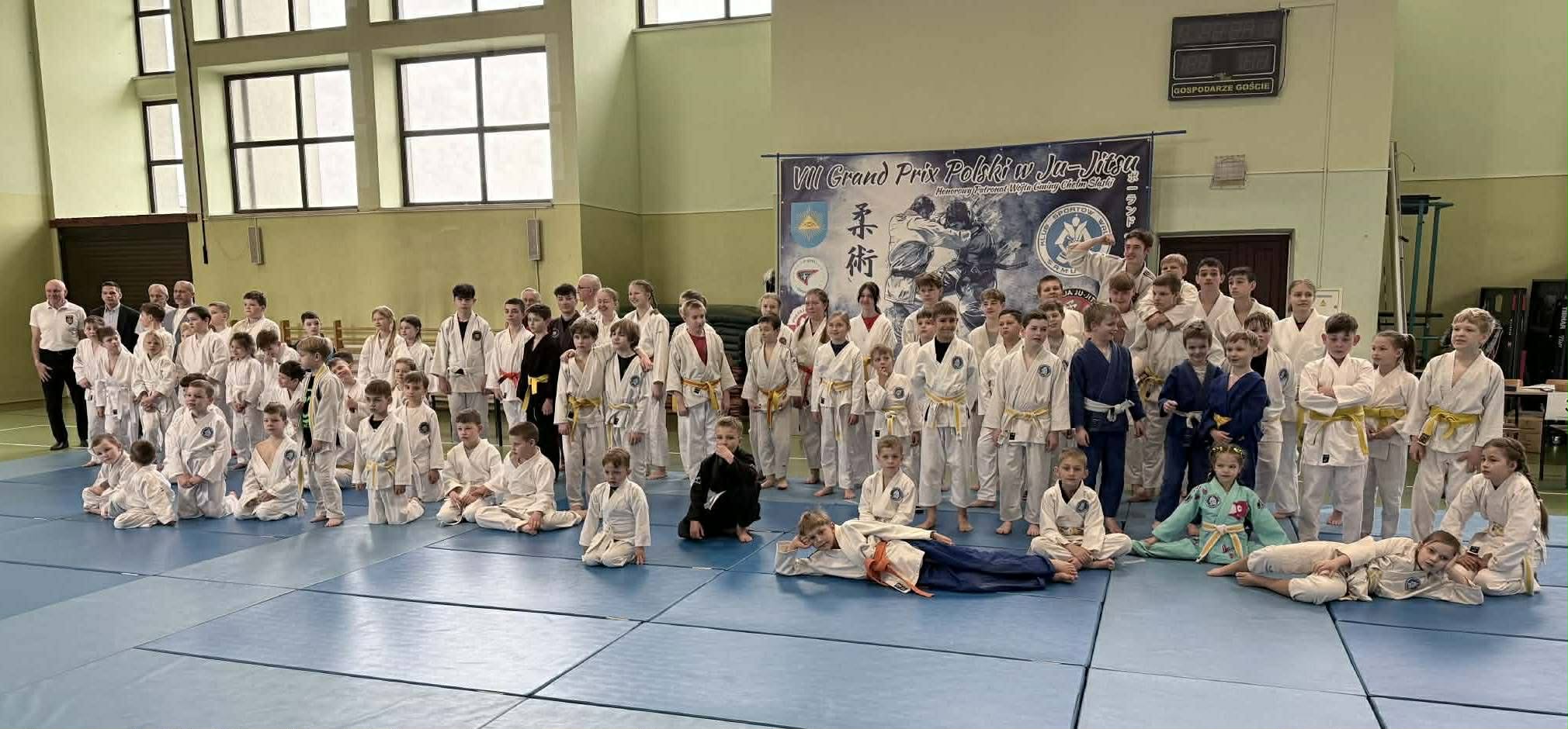 Zdjęcie uczestników turnieju w strojach sportowych w sali gimnastycznej pozujacy do grupowego zdjęcia.