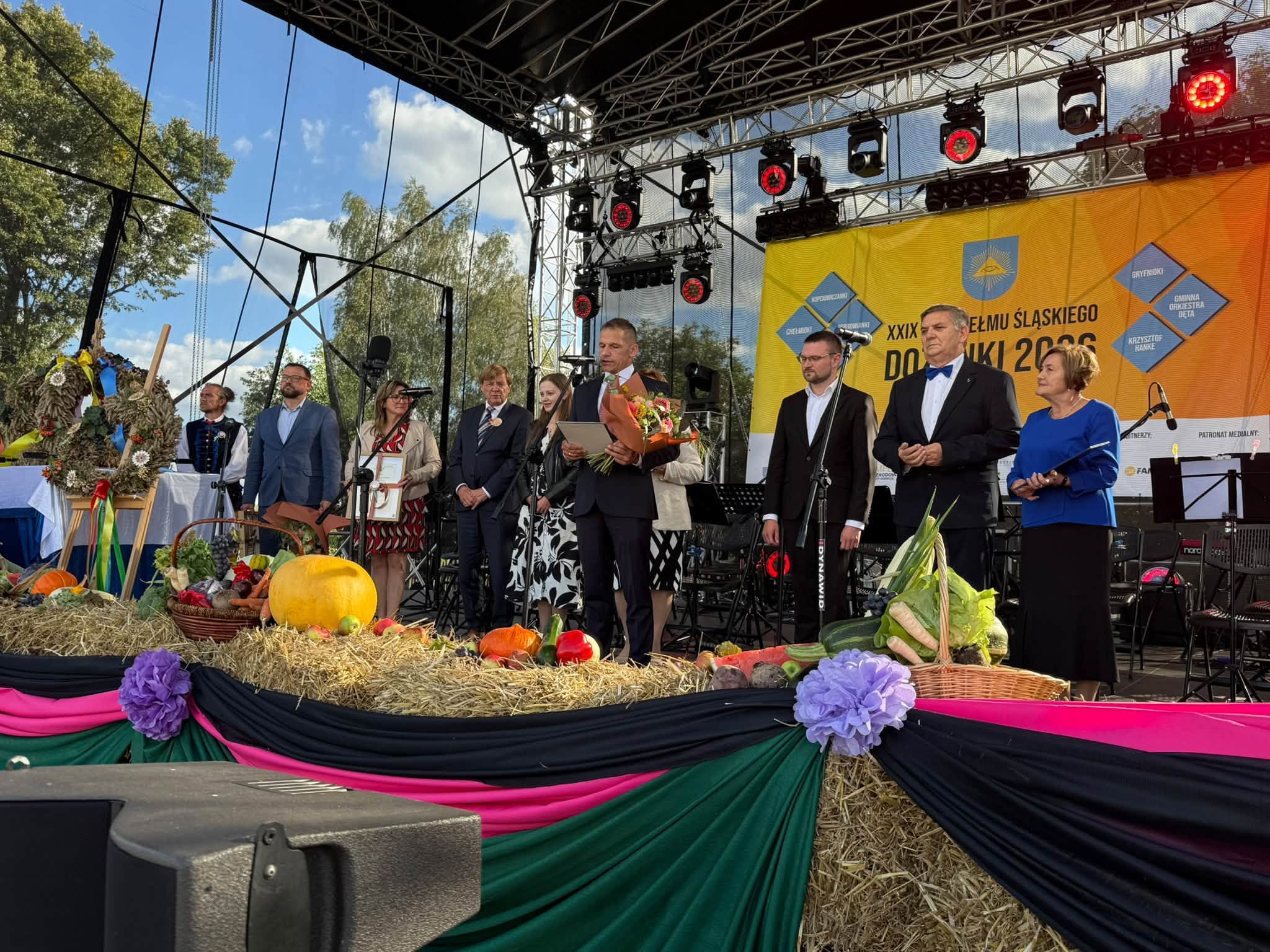 Osoby pozujące do zdjęcia na kolorowej scenie dożynkowej 