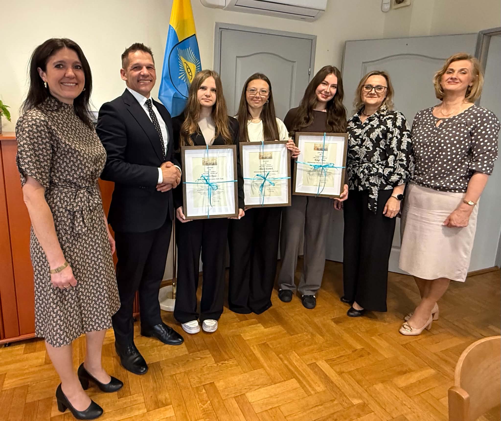 Osoby pozujące do zdjęcia w pomieszczeniu. W rękach trzymają podziekowania. 