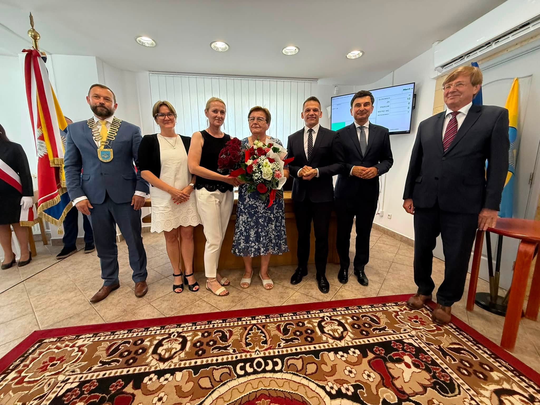 Osoby pozujące do zdjęcia w Sali sesyjnej . W tle sztandar gminy
